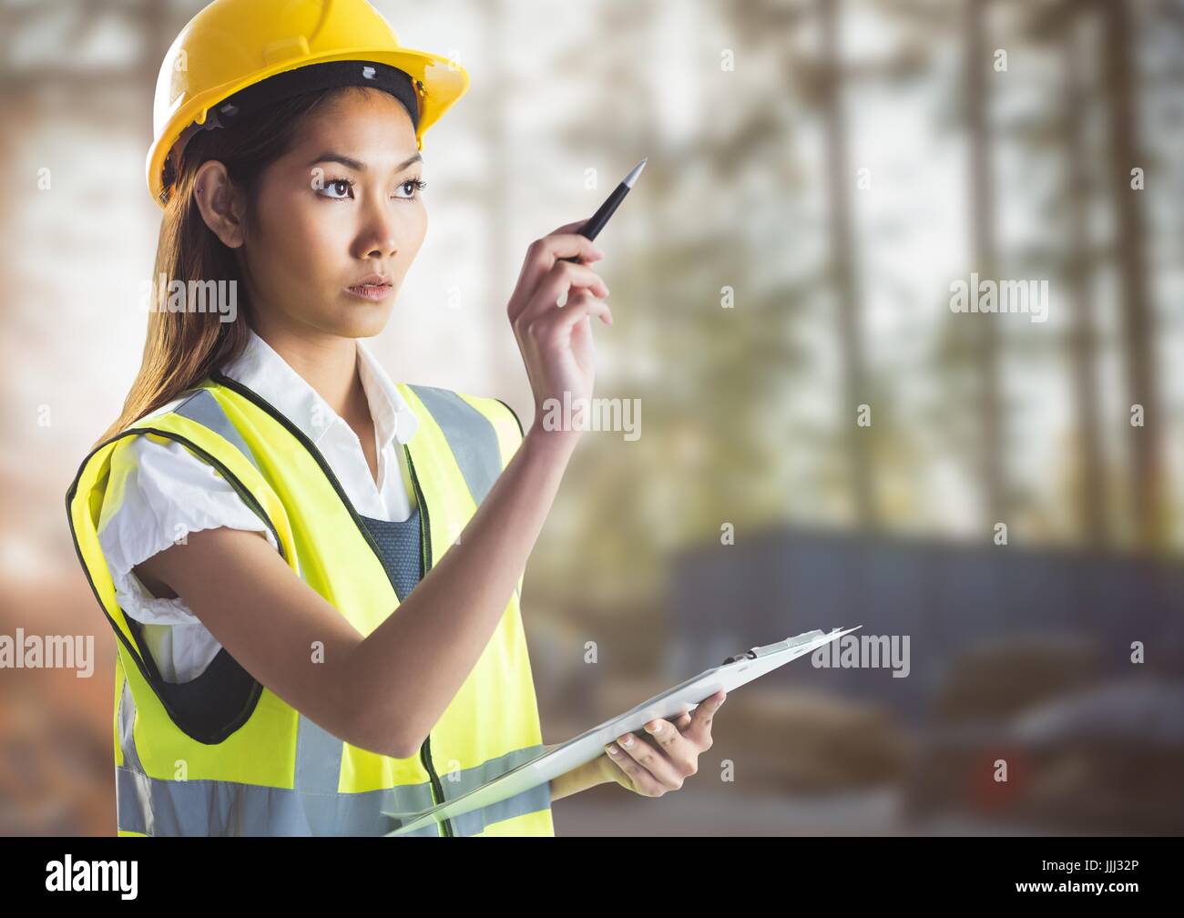Female builder with clipboard against blurry building site Stock Photo