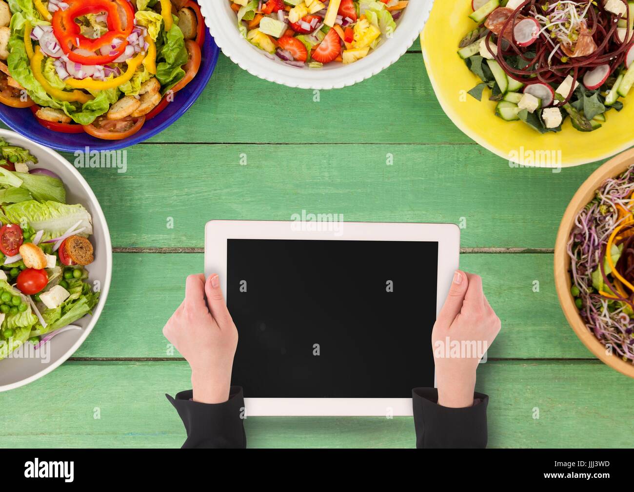 Person holding a tablet against a green wooden table with food and copy space on mobile phone Stock Photo