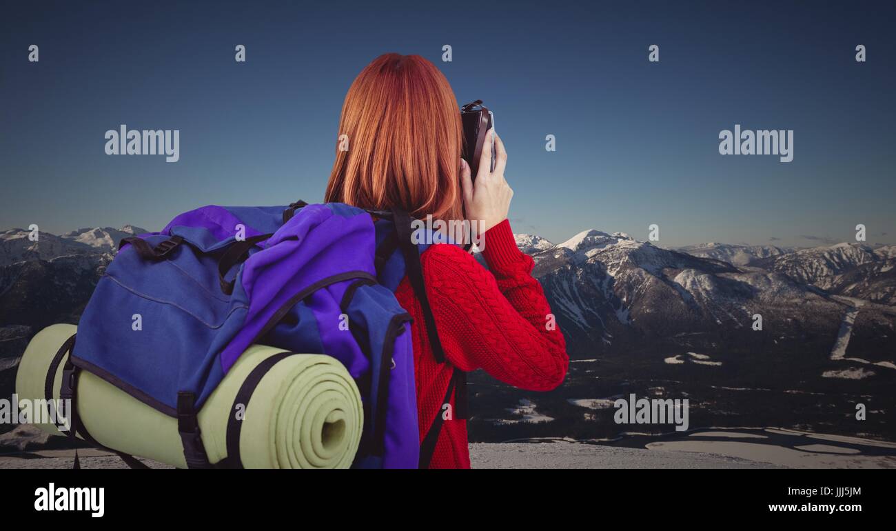 Back of millennial backpacker with camera against snowy mountain range Stock Photo