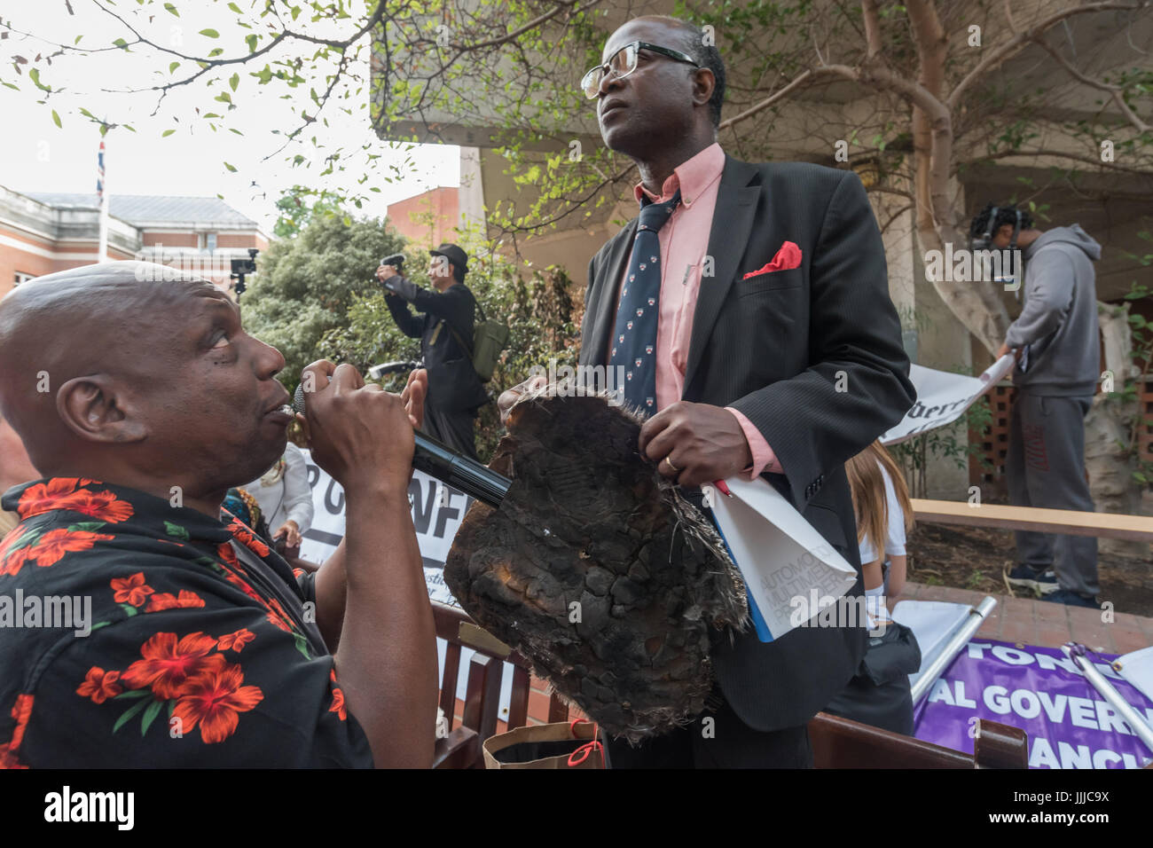 July 19, 2017 - London, UK - London, UK. 19th July 2017. A man who lost family members is introduced as he stands holding a square of the cladding from Grenfell Tower at the protest by survivors and supporters at the council meeting at Kensington Town Hall telling councillors to resign. A couple of hundred protesters attended the council meeting, though some survivors were kept outside until the residents representative refused to speak until they were allowed in and there were many empty seats, while hundreds more watched the proceedings on a giant screen outside, erupting with fury at the co Stock Photo