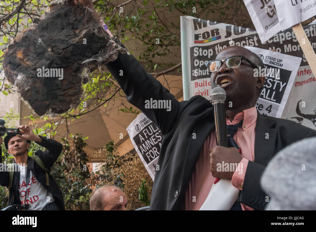 July 19, 2017 - London, UK - London, UK. 19th July 2017. A man who lost family members speaks with passion holding a square of the cladding from Grenfell Tower at the protest by survivors and supporters at the council meeting at Kensington Town Hall telling councillors to resign. A couple of hundred protesters attended the council meeting, though some survivors were kept outside until the residents representative refused to speak until they were allowed in and there were many empty seats, while hundreds more watched the proceedings on a giant screen outside, erupting with fury at the complacen Stock Photo