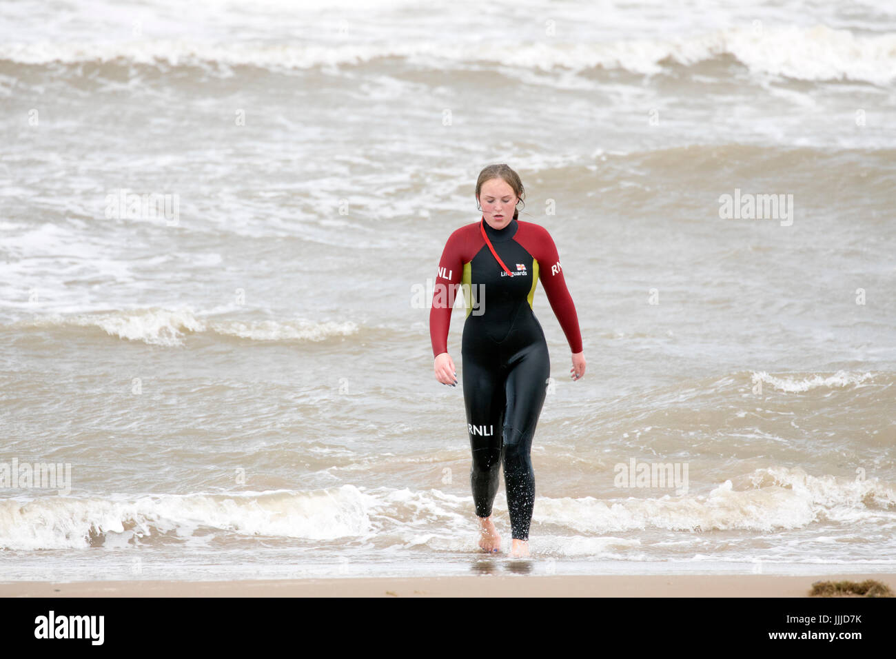 A woman RNLI life guard leaving a rough sea at Rhyl in North Wales wearing a wet suit in summer, Denbighshire, Wales, UK Stock Photo