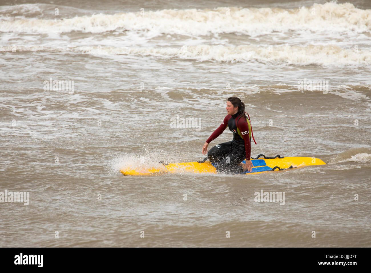 A female RNLI lifeguard practicing in the rough sea at the coastal resort town of Rhyl in Denbighsire, North Wales, UK Stock Photo