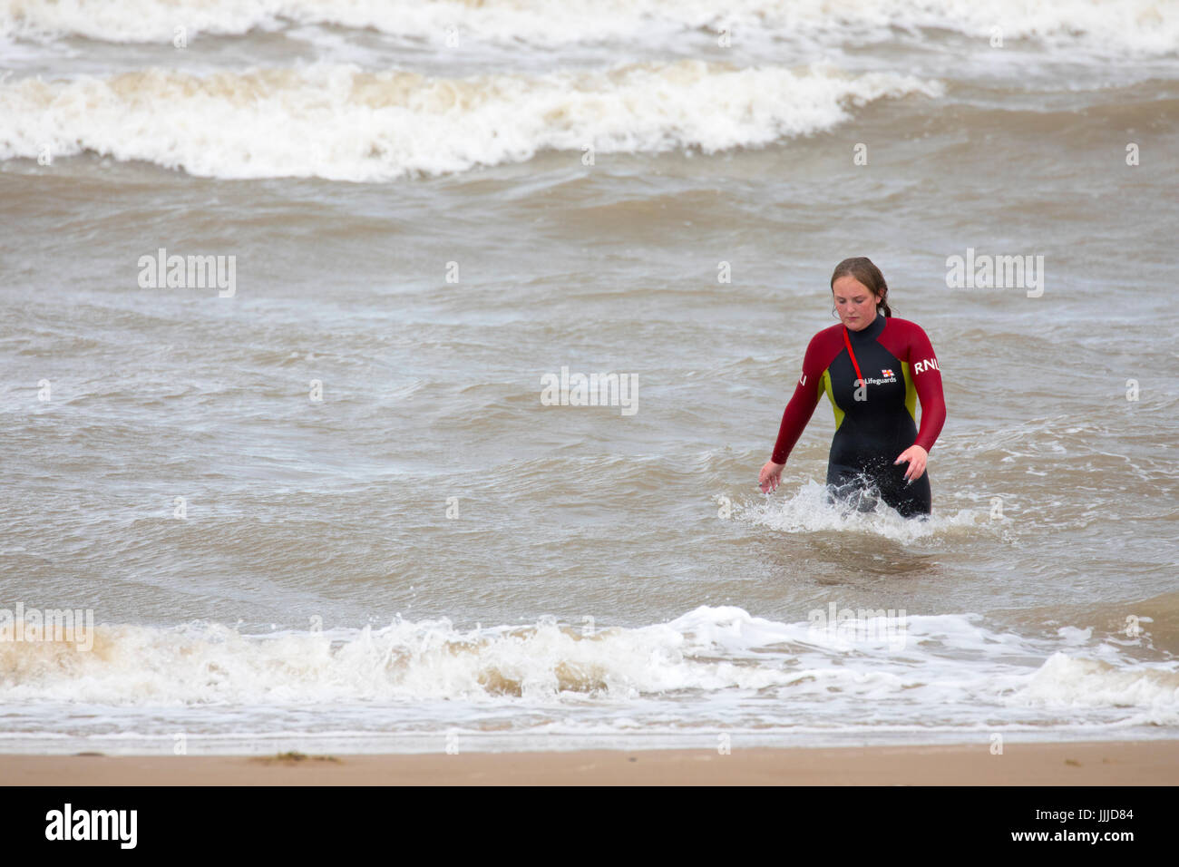 A woman RNLI life guard leaving a rough sea at Rhyl in North Wales wearing a wet suit in summer, Denbighshire, Wales, UK Stock Photo