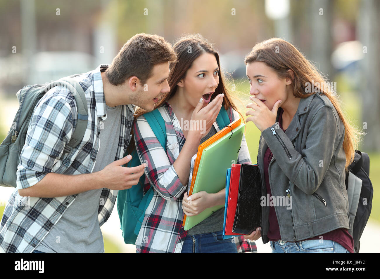 Three gossip students telling secrets in the street Stock Photo