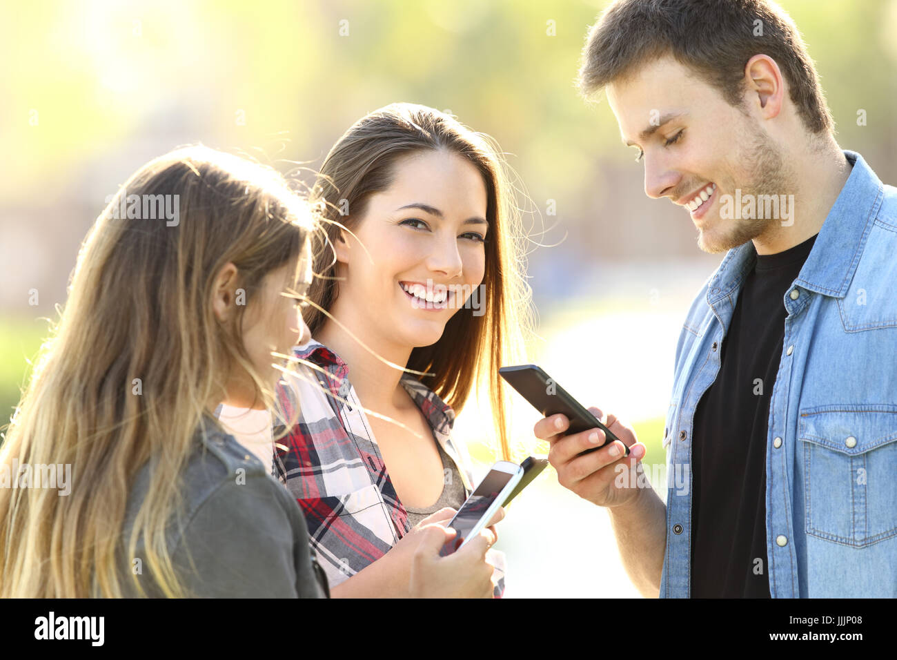 Three teens using their smart phones and one of them looking at you in the street Stock Photo