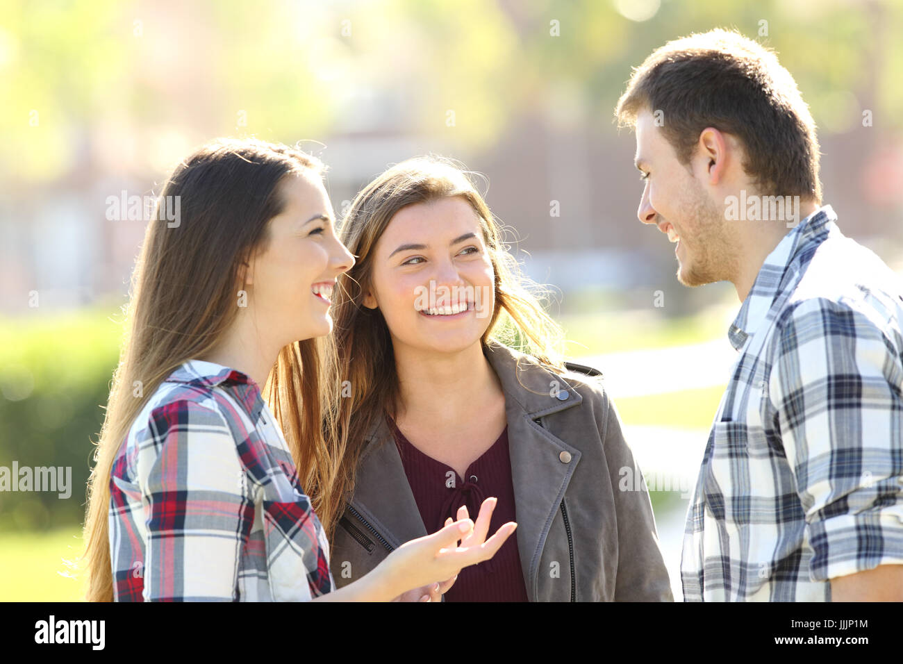 Three happy friends talking and laughing standing together in the street Stock Photo