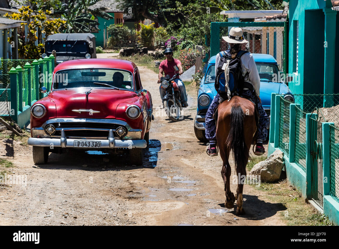 Vintage cars and horses share the road on a tour of the Vale de Silencio - VINALES, CUBA Stock Photo