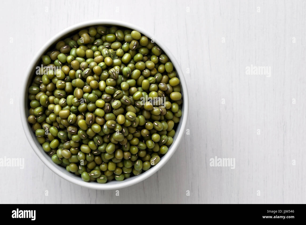 Dry mung beans  in white ceramic bowl isolated on painted white wood from above. Stock Photo