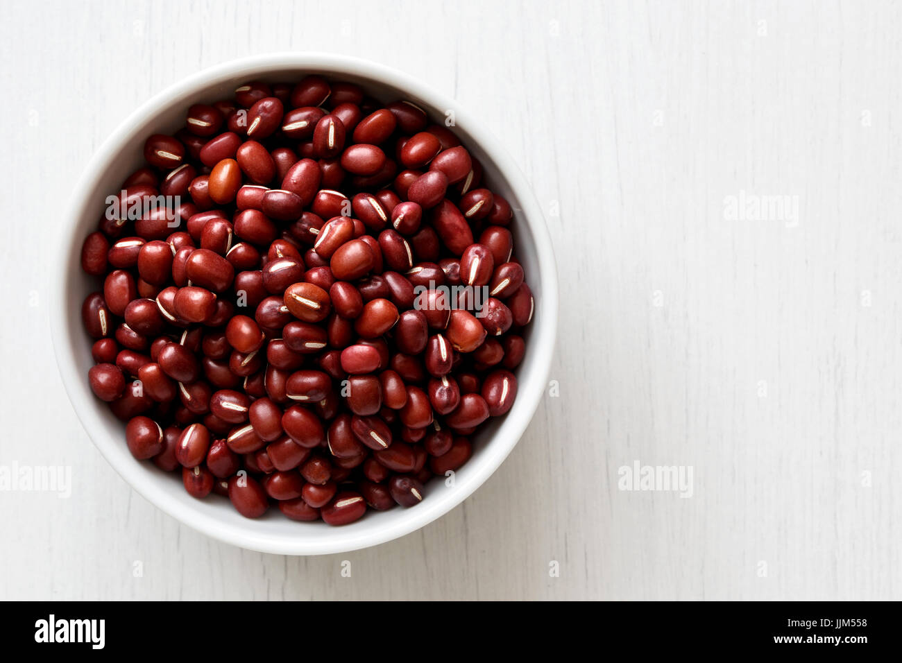 Dry adzuki beans  in white ceramic bowl isolated on painted white wood from above. Stock Photo