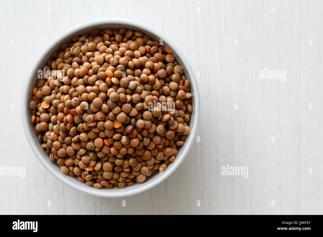 Dry unpeeled red lentils in white ceramic bowl isolated on white from above. Stock Photo