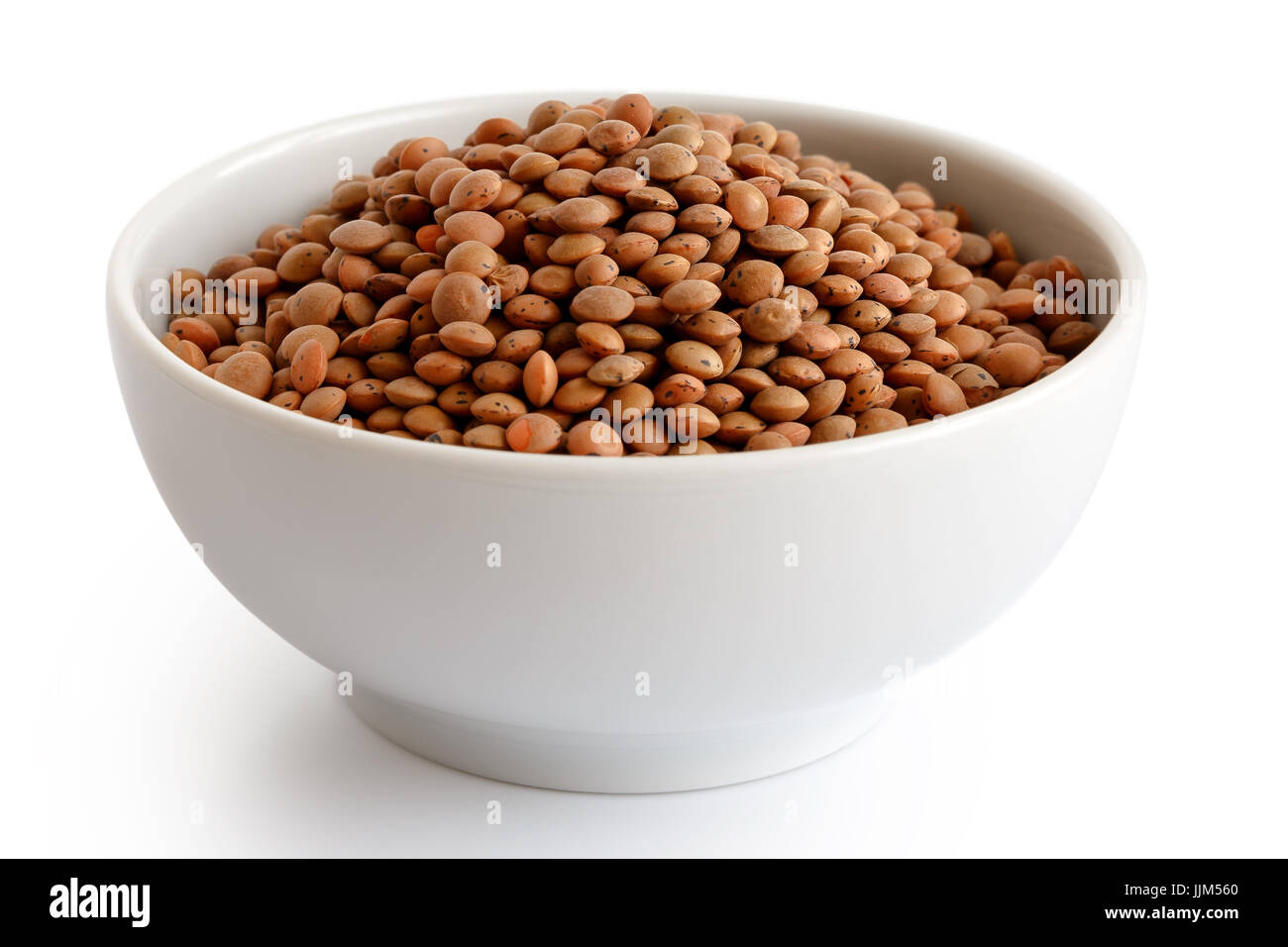 Dry unpeeled red lentils in white ceramic bowl isolated on white. Stock Photo