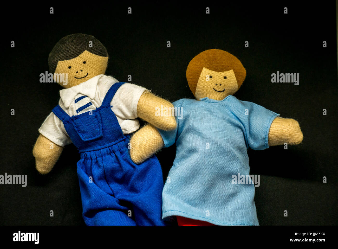 Still life of male and female toy dolls against black background to