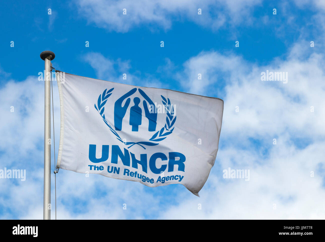 Flag of the United Nations High Commissioner for Refugees (UNHCR) waving in the wind at the UNHCR headquarters  against a blue sky with clouds. Stock Photo