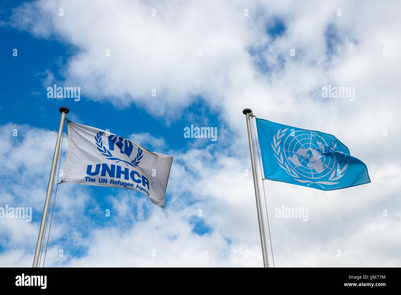 Flags of the United Nations (UN) and the United Nations High Commissioner for Refugees (UNHCR)  against a blue sky with clouds. Stock Photo