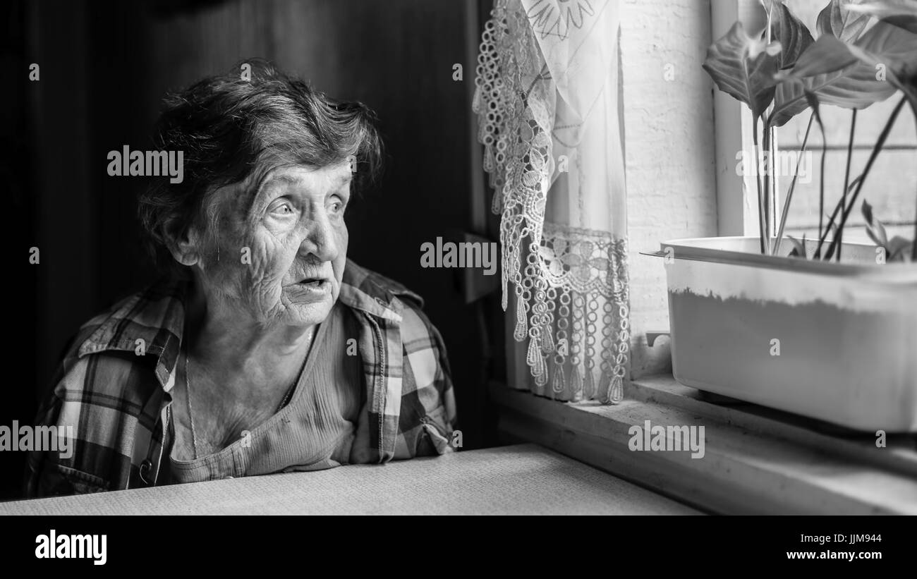 Elderly woman grieves near the window, genre photography in black and white. Stock Photo
