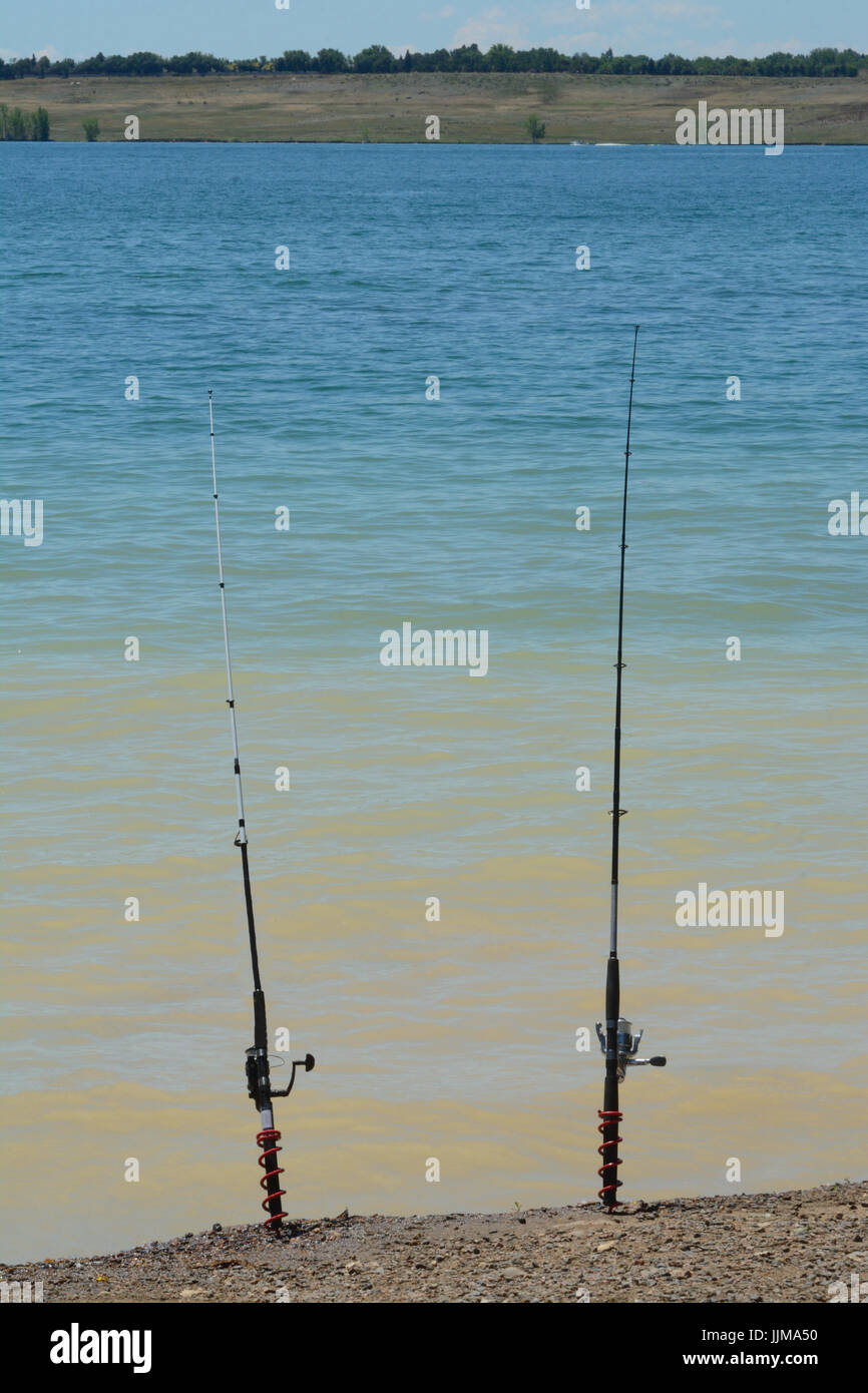 Two fishing rods held in ground of lake shore while fishermen rest or eat Stock Photo