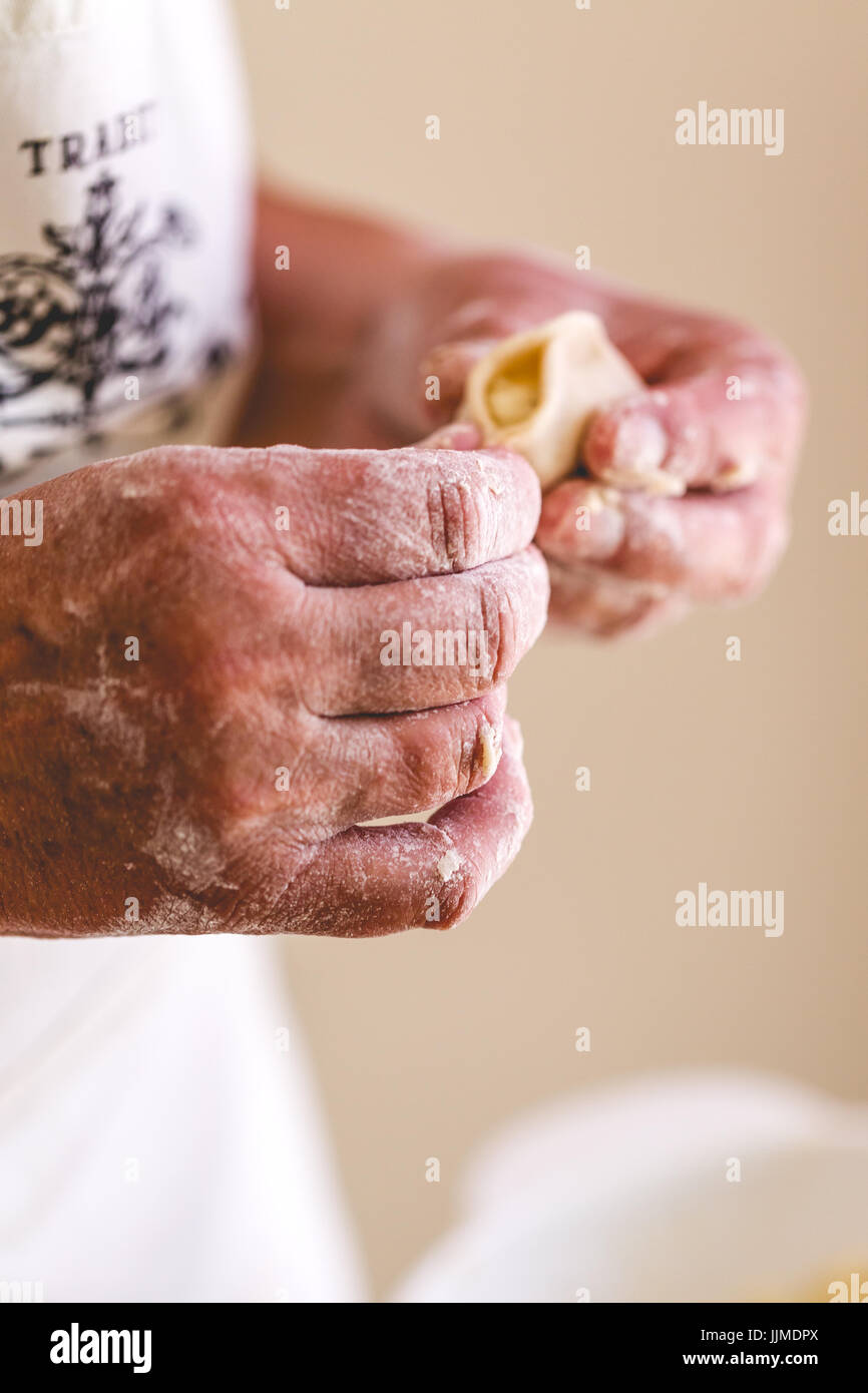 Senior woman, grand mother cooking traditional dumplings. Vertical crop, focus on hands with dumplings and stuffing Stock Photo