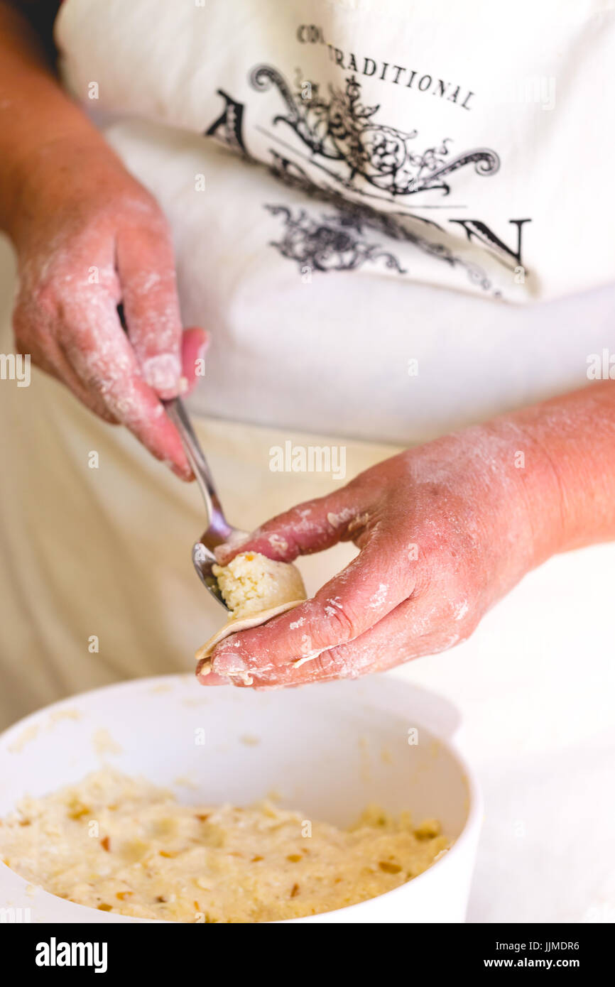 Senior woman, grand mother cooking traditional dumplings. Vertical crop, focus on hands with dumplings and stuffing Stock Photo