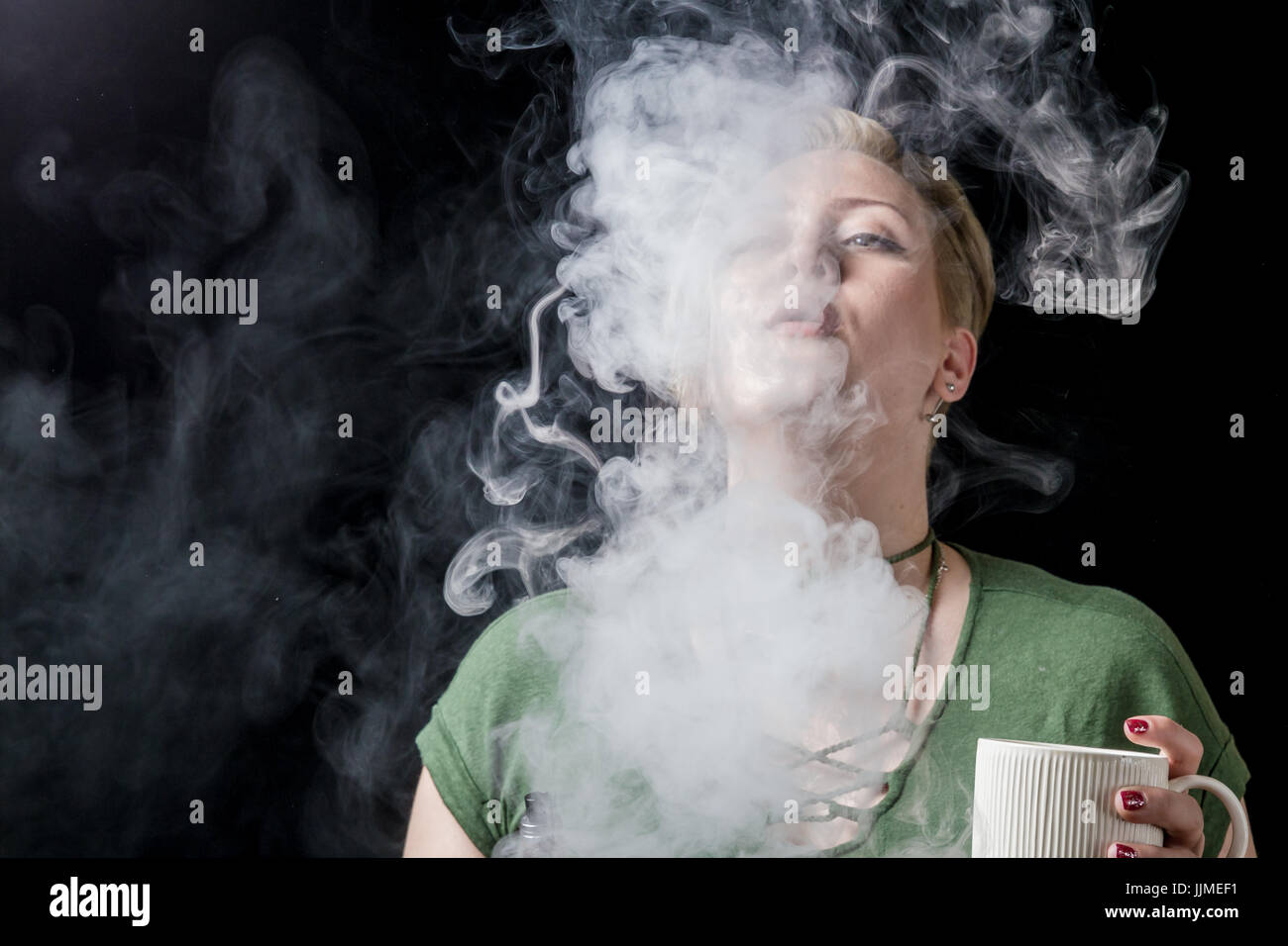 Young adult female exhaling smoke clouds from electronic cigarette Stock Photo