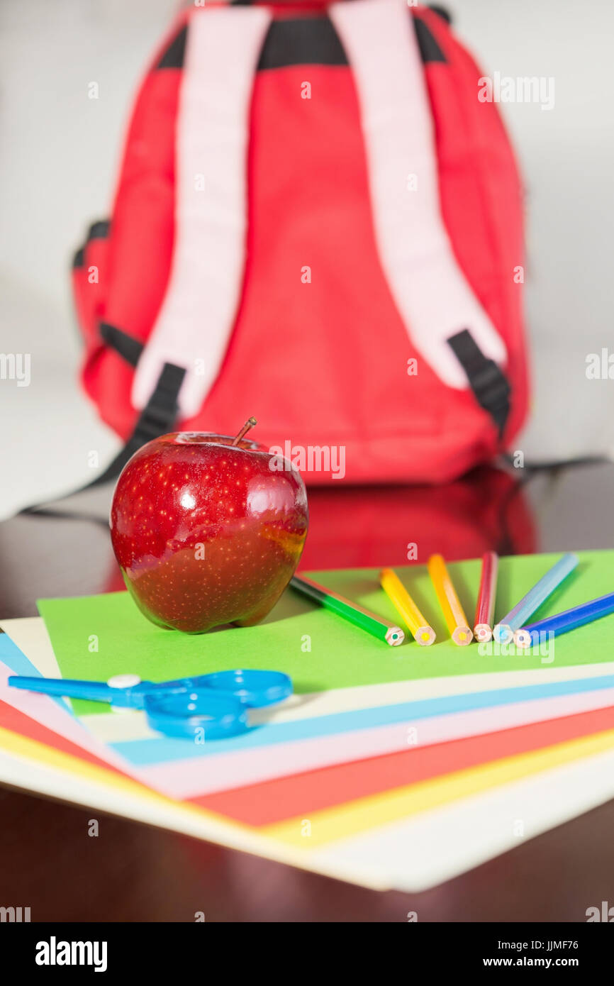 Apple and School Supplies with Red Backpack in the Background Stock Photo
