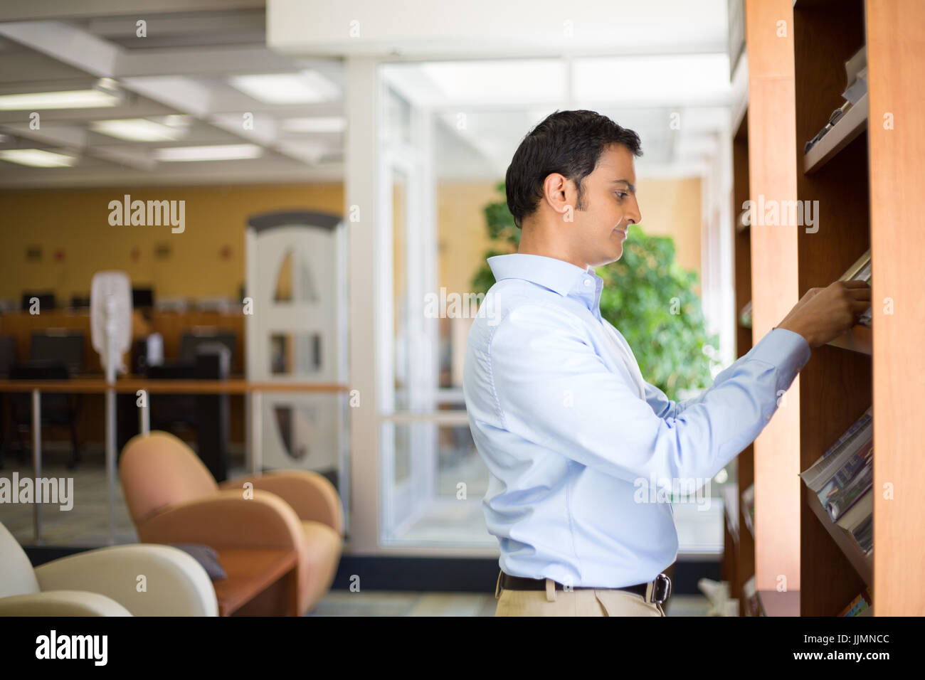 Closeup portrait, young business man in blue shirt reading, perusing books, magazines, and periodicals at library background Stock Photo