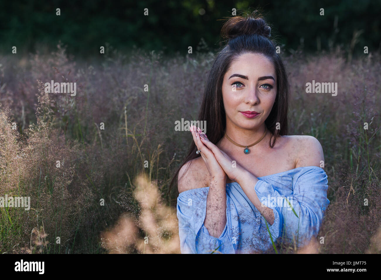 A young woman clasps the palms of her hands together during a summer evening in a grass meadow near Liverpool. Stock Photo