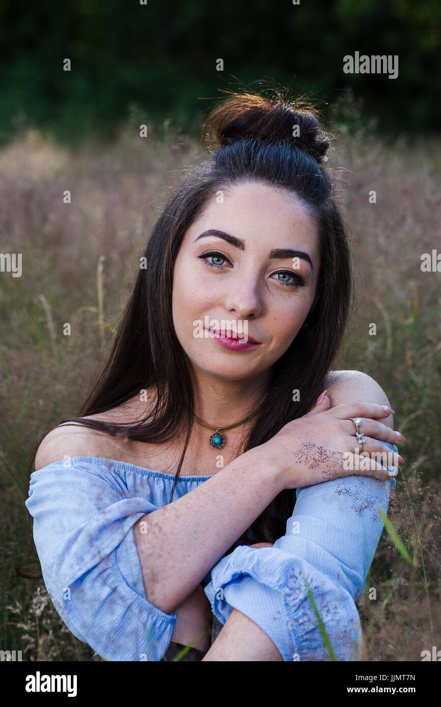 My friend crosses one arm over her chest as she faces the camera during a portrait in a meadow of long grass near Liverpool. Stock Photo
