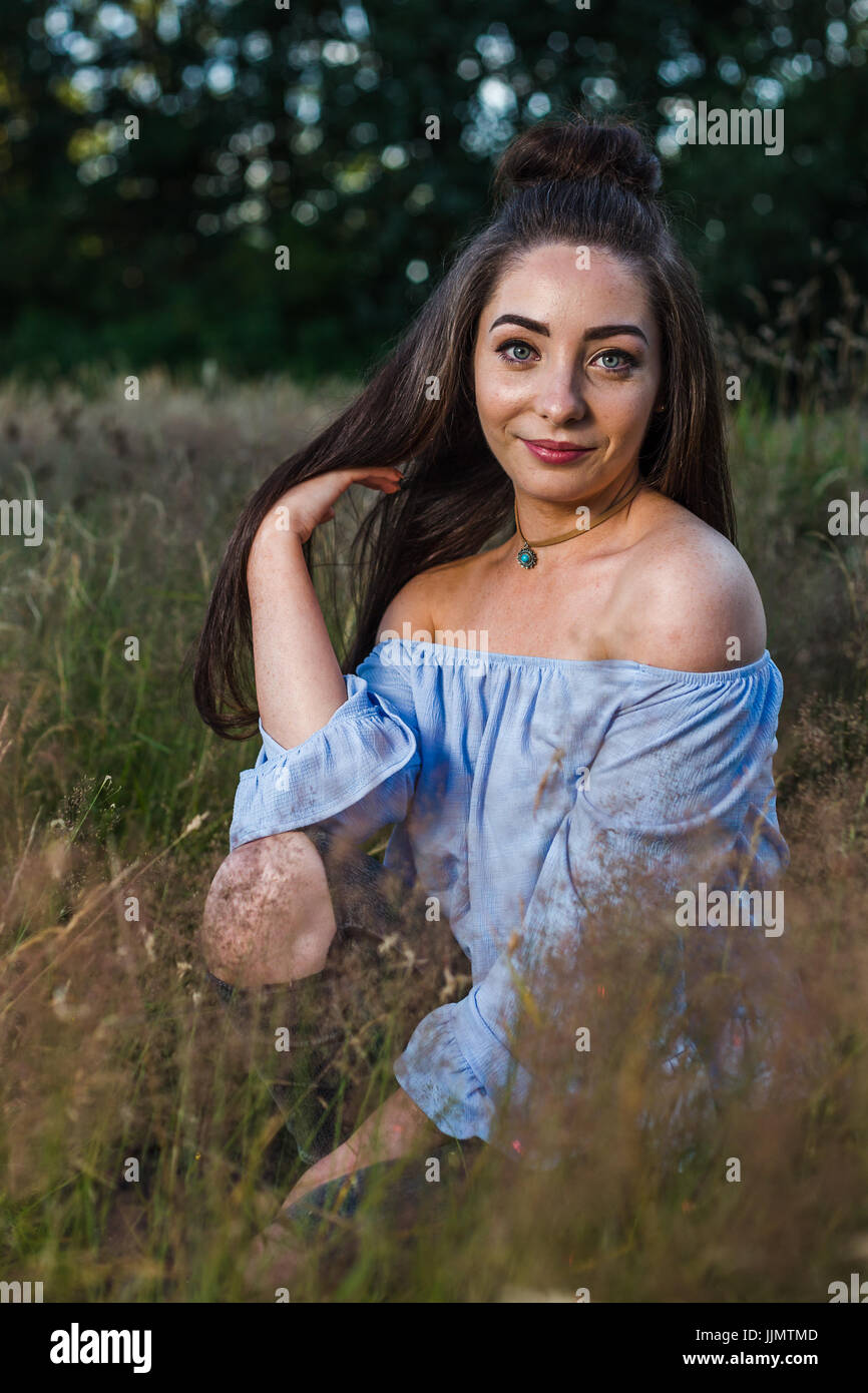 My friend runs her hand through her hair whilst kneeling on one leg during an outdoor portrait session near Liverpool one summers evening. Stock Photo