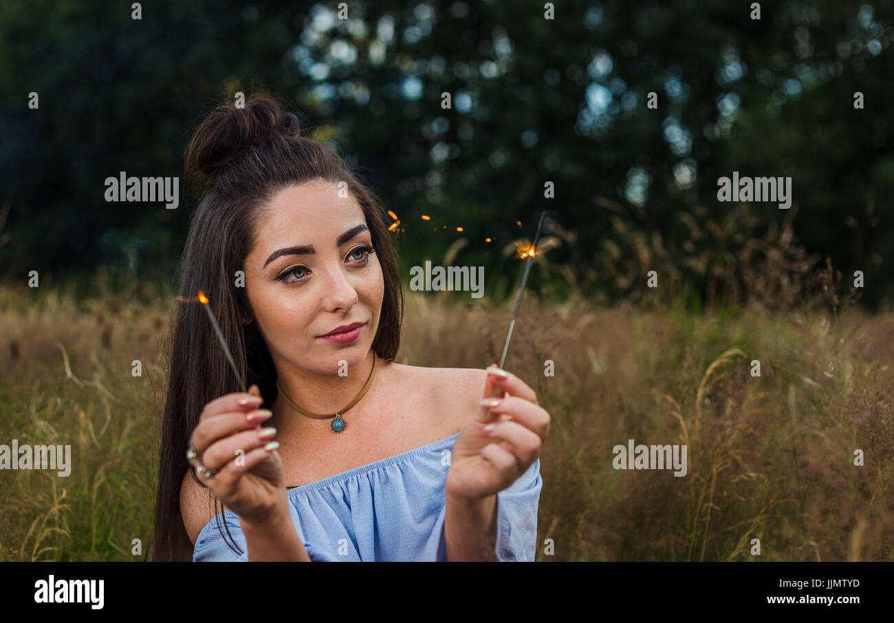 A pretty young woman watches the sparks from a sparkler during an