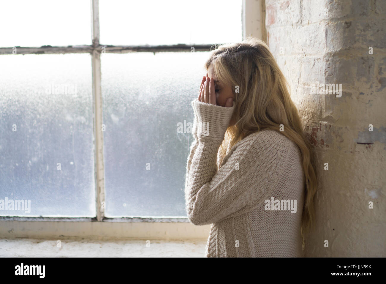 Miserable woman hiding face with hands crying by the window Stock Photo