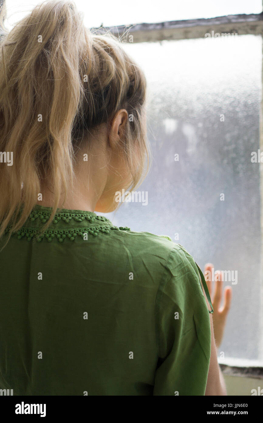 Rear view of a young blond woman standing by the window Stock Photo - Alamy