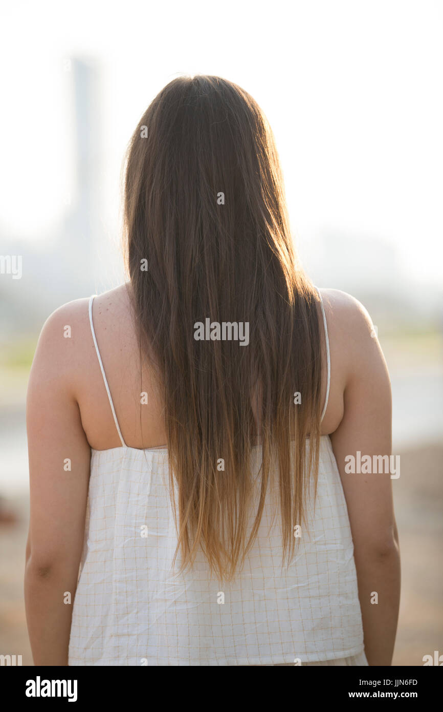 Rear view of a young woman with long dark hair standing outdoors Stock ...