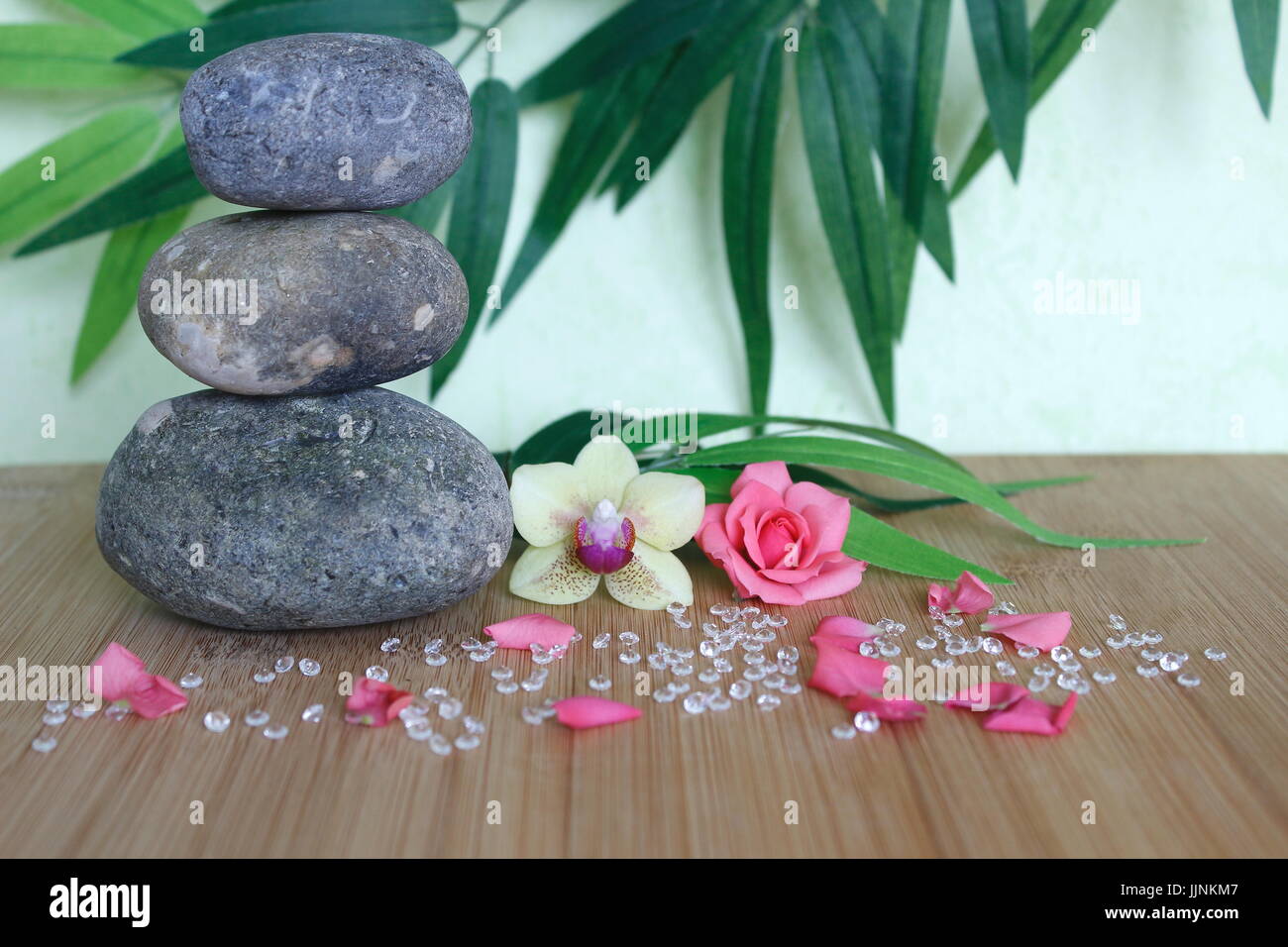 Decorative pebbles stacked in a Zen life fashion on a bamboo wooden board  with a pink flower and an orchid on a green and foliage background Stock Photo