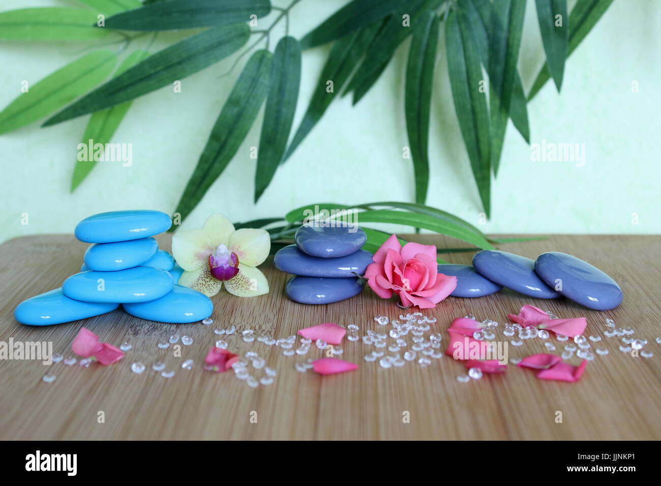 Decorative pebbles stacked in a Zen life fashion on a bamboo wooden board  with a pink flower and an orchid on a green and foliage background Stock Photo