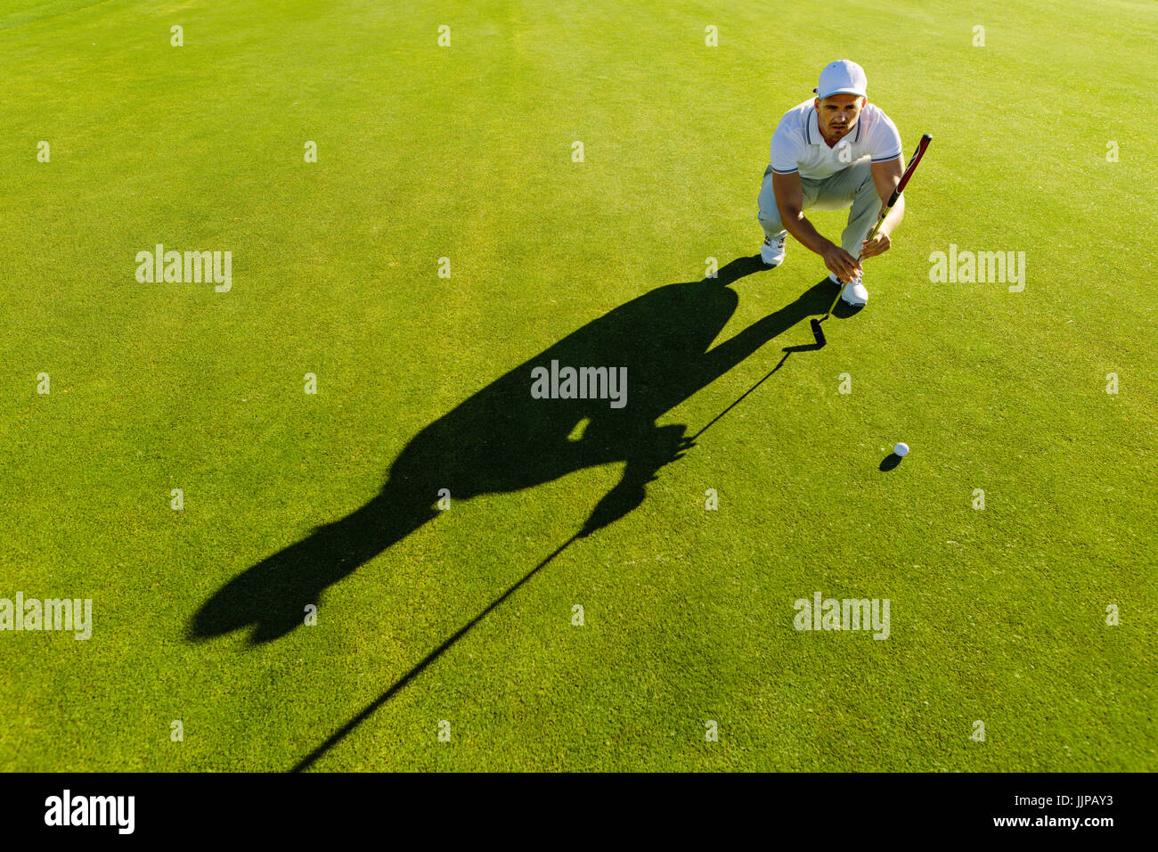 Golf player aiming shot with club on course. Male golfer check line for putting golf ball on green grass. Stock Photo