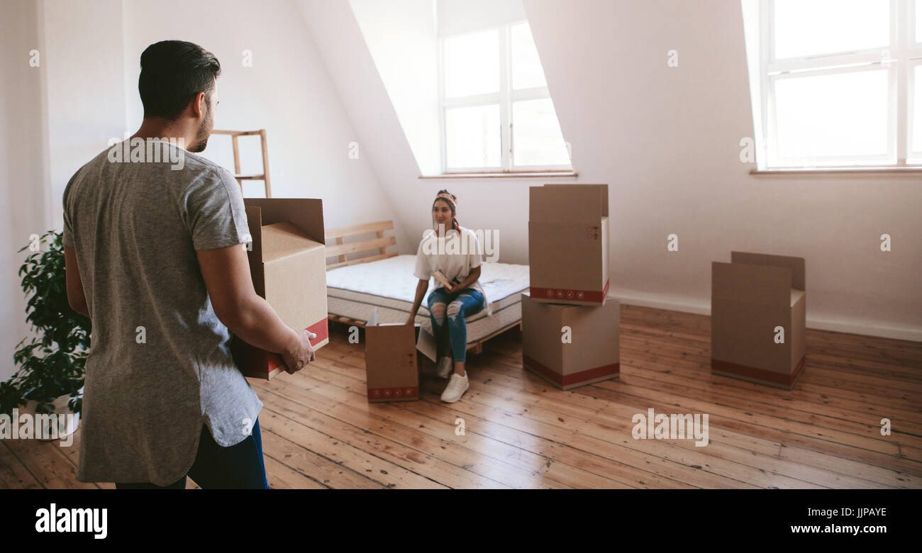 Indoor shot of young woman sitting on bed with man carrying box in new