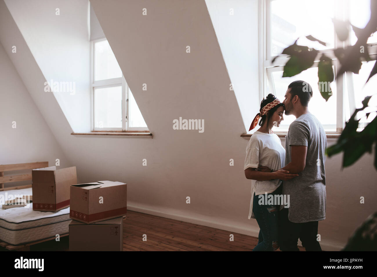 Indoor shot of loving young couple moving into their new home. Man and woman in love standing together with cardboard boxes in room. Stock Photo