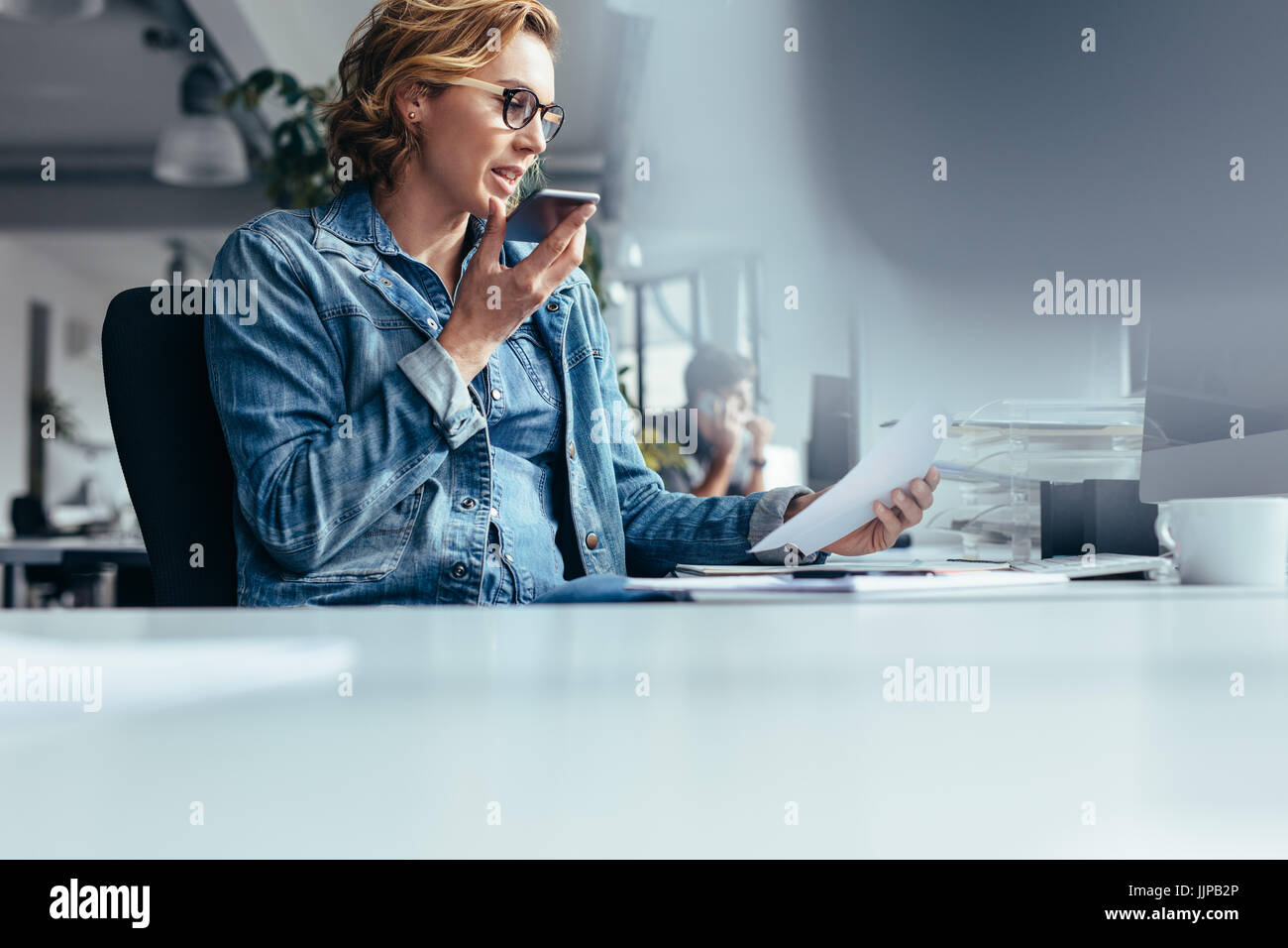 Young Businesswoman Talking On Speaker Phone With Document Young