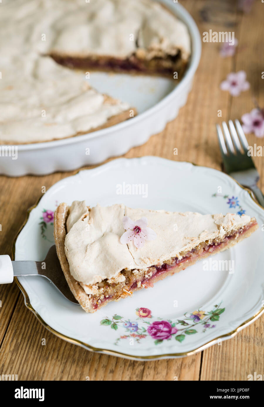 Close up of almond pie topped with meringue arranged on a flowery plate and old wooden table Stock Photo