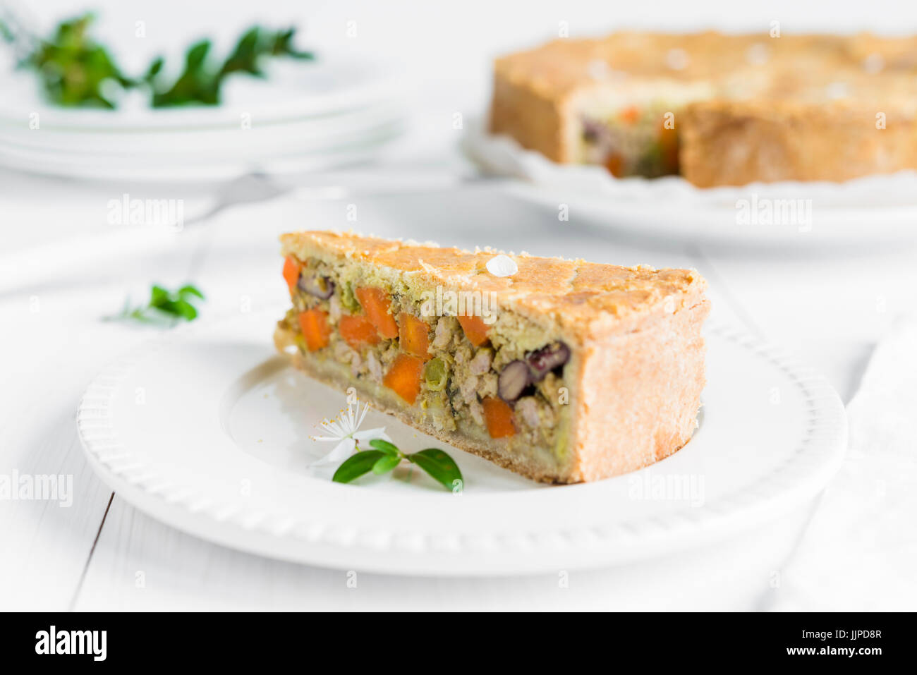 Closeup of a piece of meat pie baked with vegetables, carrots, red beans and peas arranged on white plate and wooden table Stock Photo