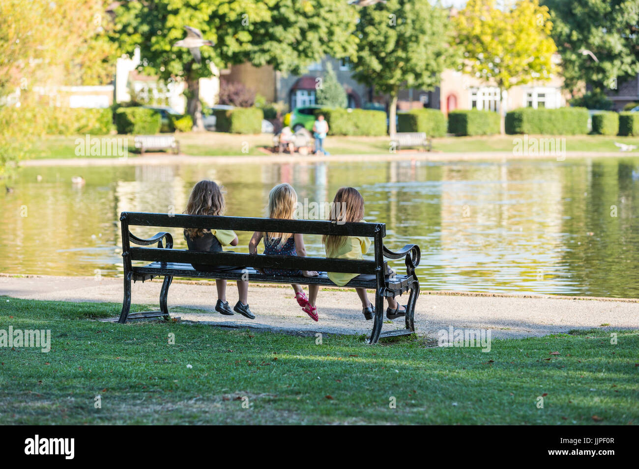 Three Children Sat Together On A Park Bench In Memorial Park In