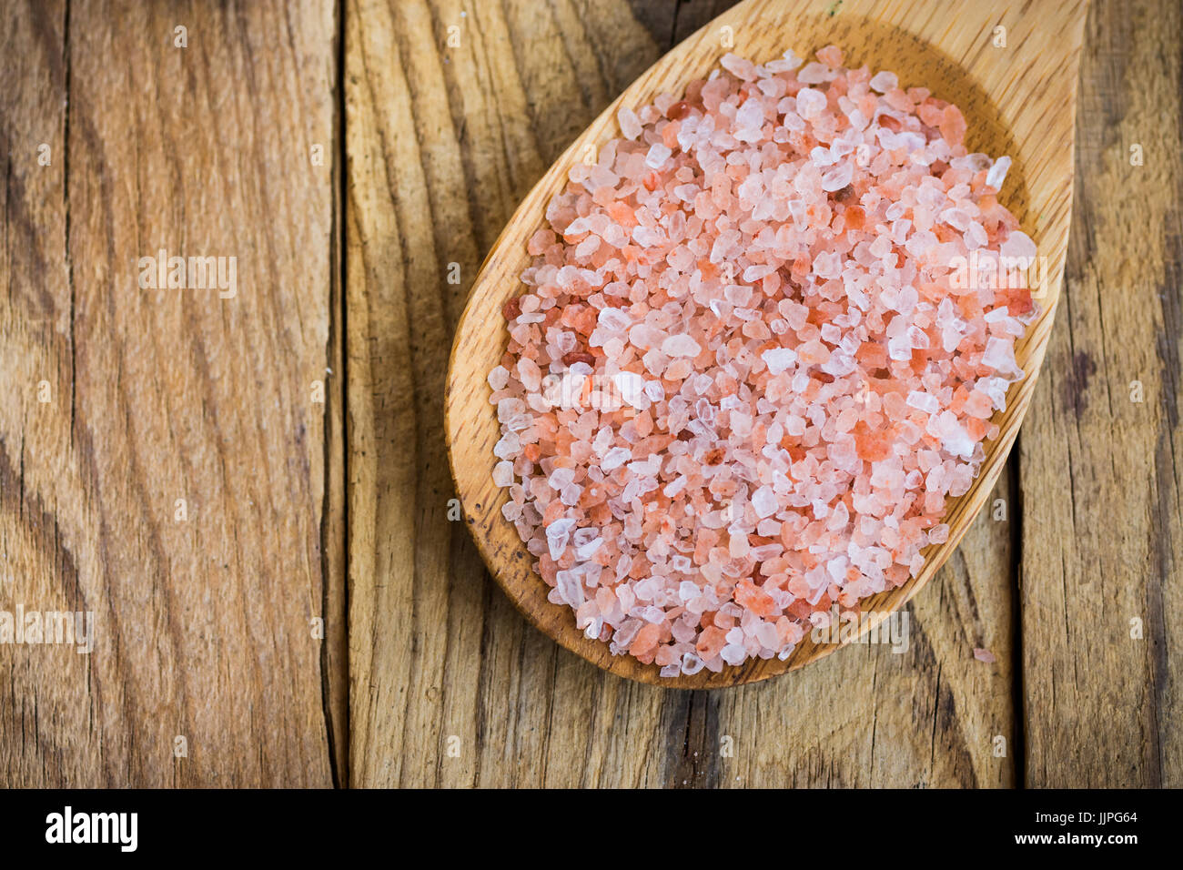 Pink Himalayan salt in wooden spoon on plank wood background, healthy