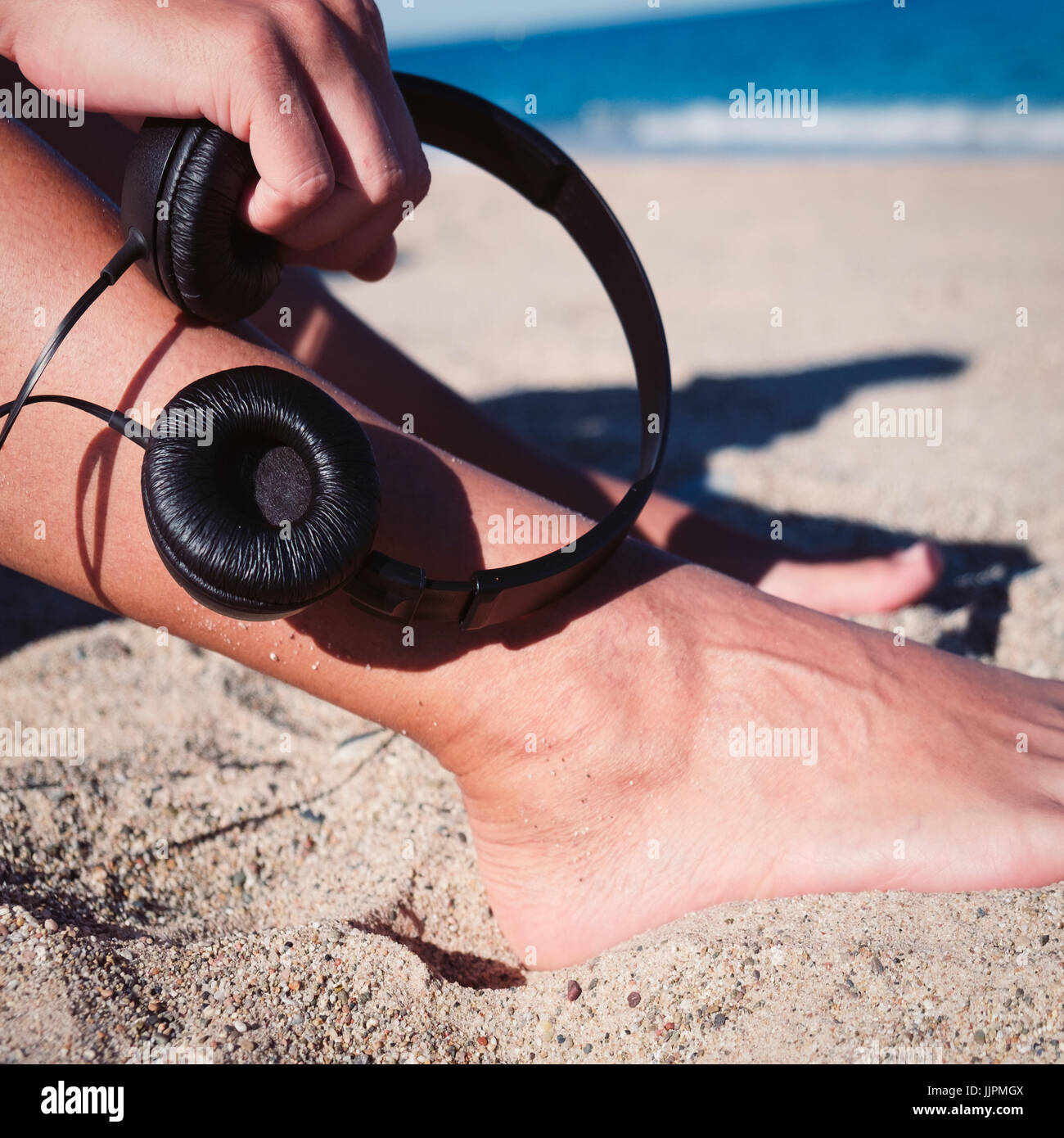 closeup of a young man holding a pair of headphones in his hand sitting in the sand of the beach Stock Photo
