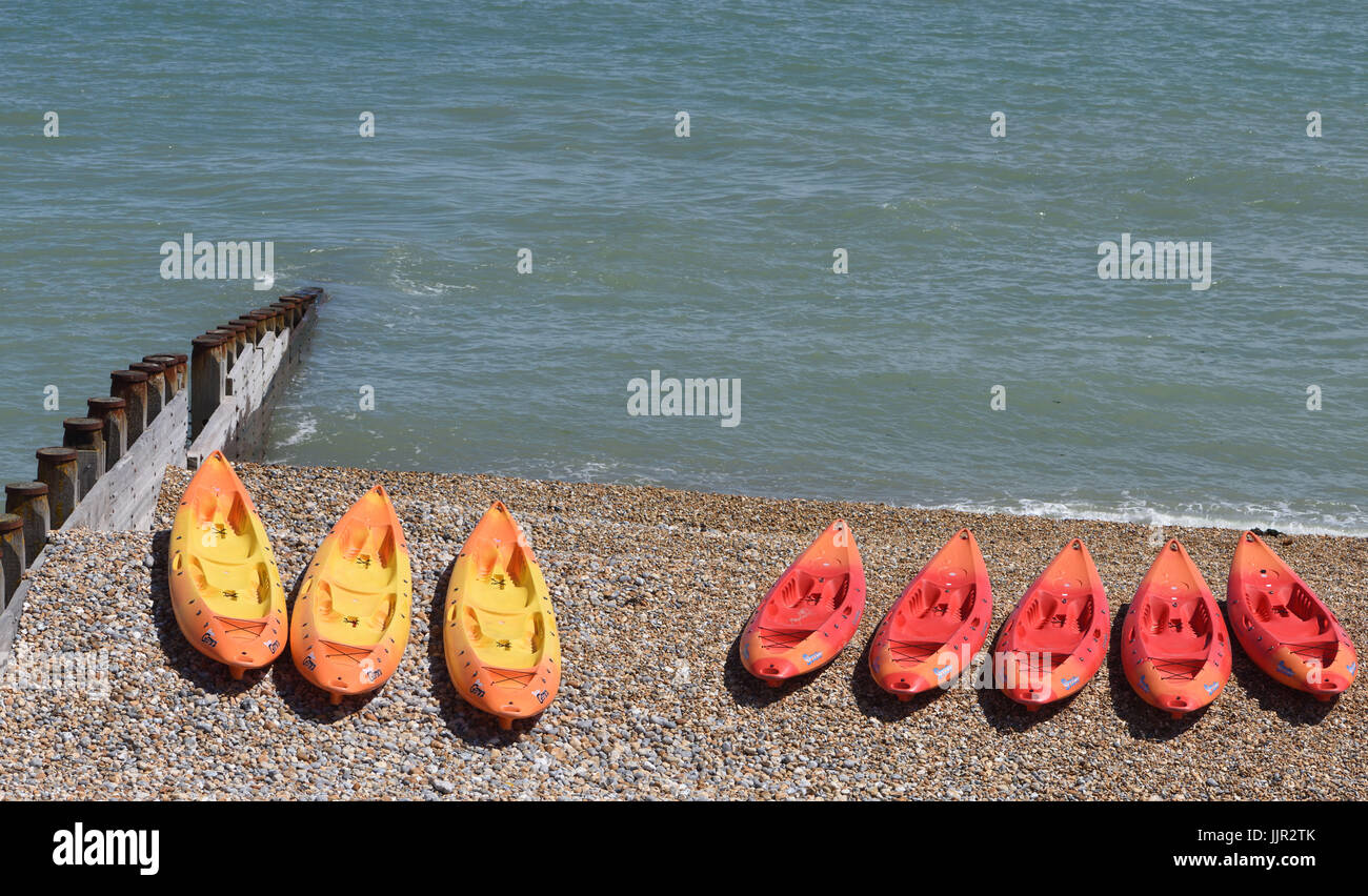 Brown and red canoes on the shingle beach at Eastbourne. Eastbourne, Sussex, UK. Stock Photo