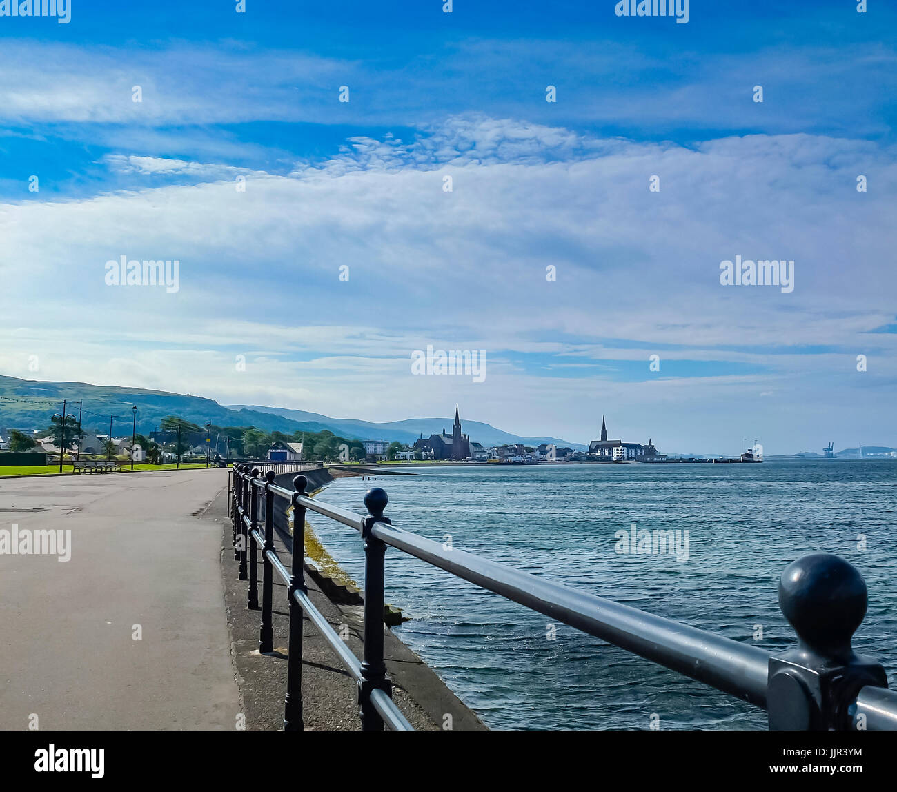 Looking south along the railings into largs towards the town centre at the paddle steamer and car ferry. Hunterston Wind turbines in the distance. Stock Photo
