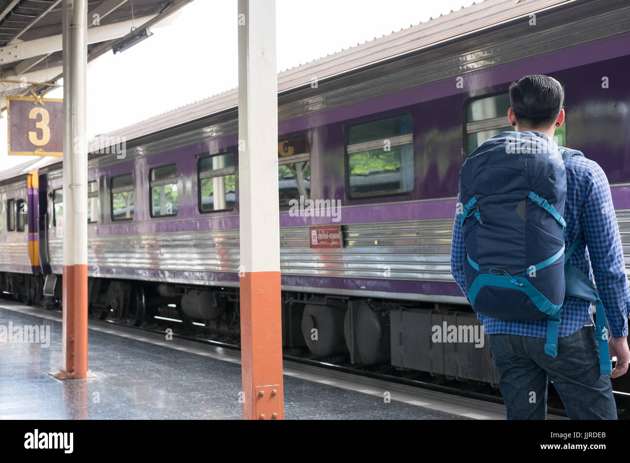 young asian man with backpack standing on platform at train station ...