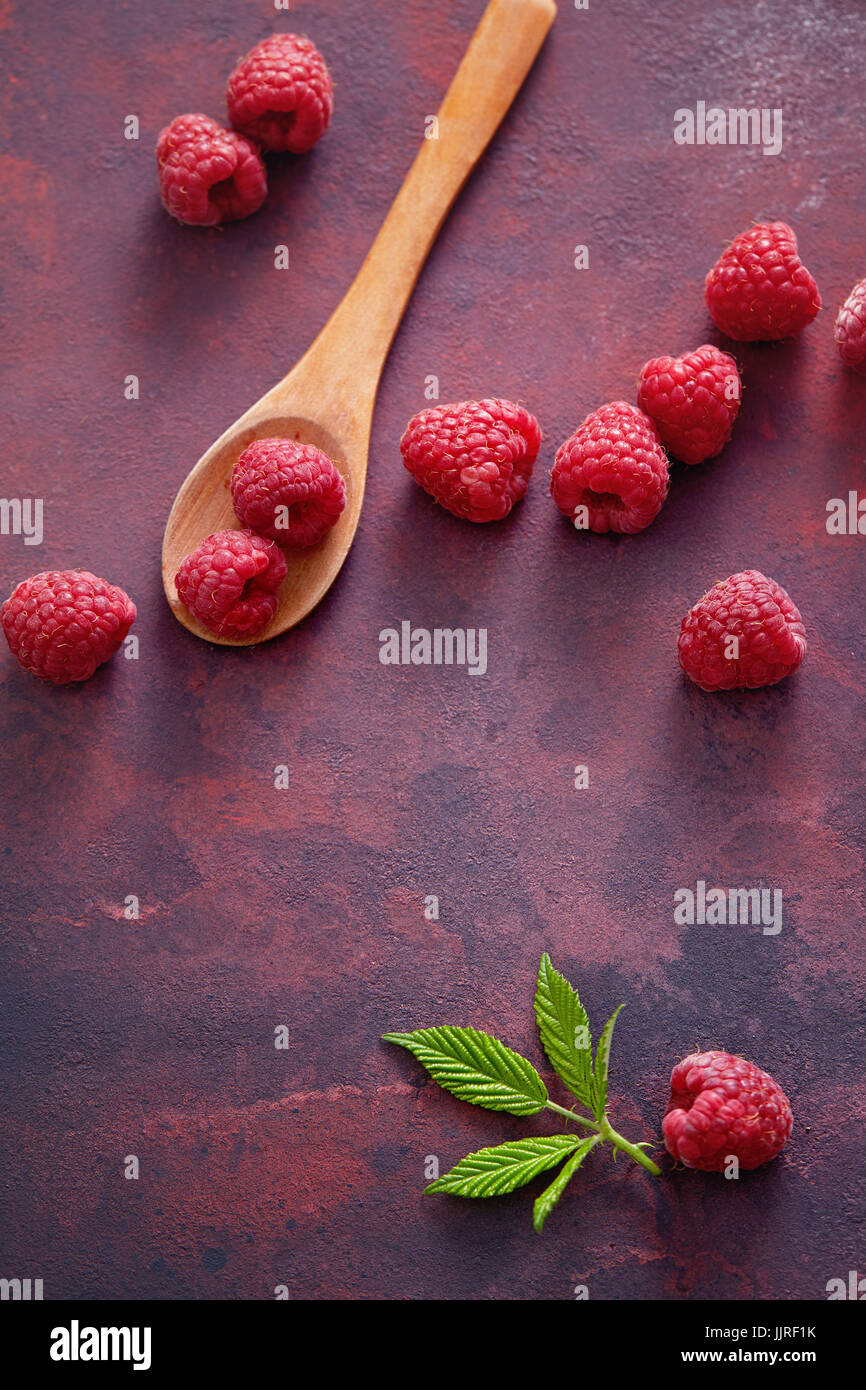 A fresh raspberry on a wooden spoon. Ripe fresh raspberries with leaves on rustic background. Stock Photo