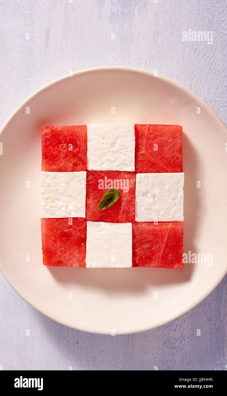 Cubes of watermelon and feta cheese on a plate forming a square pattern with mint leaves Stock Photo