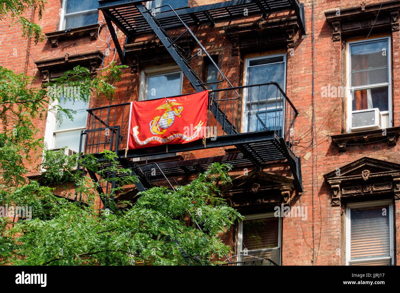 Red, gold and white United States Marine Corps flag on a fire escape in a Lower Manhattan tenement building in New York City Stock Photo